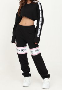 Svart kort sweatshirt med långa ärmar och vita logoband. Svarta joggers med rosa band med ögon grafik och stjärnor. Vita sneakers.