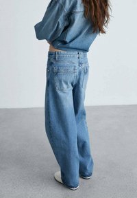 Blugi de culoare albastră deschisă, cu talie înaltă și croială relaxată, dotati cu buzunare la spate și o ușoară decolorare, asortați cu un top din denim.