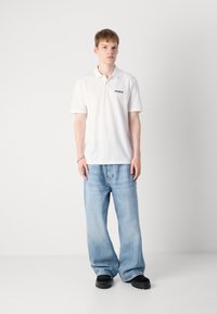 Hvit polo skjorte med kort erme og en svart "HUGO" logo på brystet, sammen med avslappede lys blå denimjeans og svarte sko.