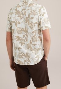 Short-sleeve, light-colored shirt with a beige leaf pattern; paired with dark brown shorts, showing a relaxed, casual fit.