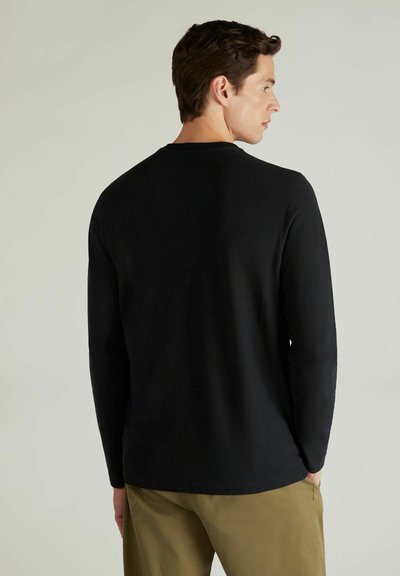 Schwarzes Langarmshirt aus glattem Stoff, mit Rundhalsausschnitt und geradem Saum, getragen mit hellen Hosen.