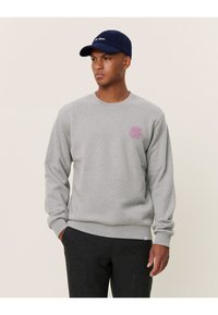 Szary sweatshirt wykonany z materiału bawełnianego, z okrągłym dekoltem i małym różowym okrągłym logo po lewej stronie klatki piersiowej.