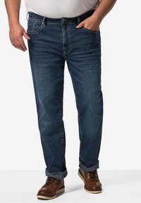 Dunkelblaue Jeans aus Denim mit geradem Schnitt, heller Naht und umgeschlagenen Bündchen. Kombiniert mit braunen Schnürstiefeln für einen vollständigen Look.