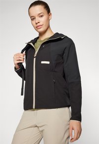 Veste zippée noire et grise avec capuche, ornée d'une accent crème le long de la fermeture éclair et du logo, fabriquée en tissu doux et texturé.