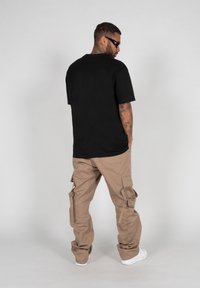 Schwarzes Baumwoll-T-Shirt mit lockerem Schnitt, kombiniert mit khakifarbener Cargo-Hose mit mehreren Taschen und schmal zulaufendem Bein, abgerundet mit weißen Sneakers.