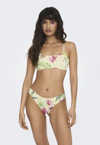 Ensemble bikini floral en jaune pastel avec des motifs tropicaux roses et verts. Haut de style bralette avec des fines bretelles, bas taille basse assortis.