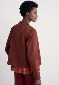 Raundzelt värvi jope, millel on mugav lõige, kaelus, tasku ja soojades toonides kihtidega ruuduline särk aluses. Pehme puuvillase materjal.