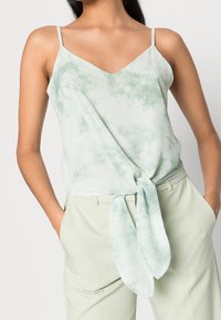 Jasnozielony top z wiązaniem z przodu, dekoltem w serek i cienkimi ramiączkami, wykonany z miękkiego, delikatnego materiału o subtelnym wzorze tie-dye.