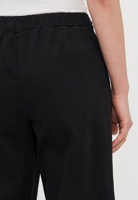 Black trousers with an elastic waistband, featuring a smooth texture and no visible patterns. The back shows a relaxed fit.