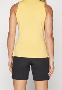 Haut sans manches jaune en tissu léger, associé à un short noir. Le haut présente un col rond et une coupe ajustée.