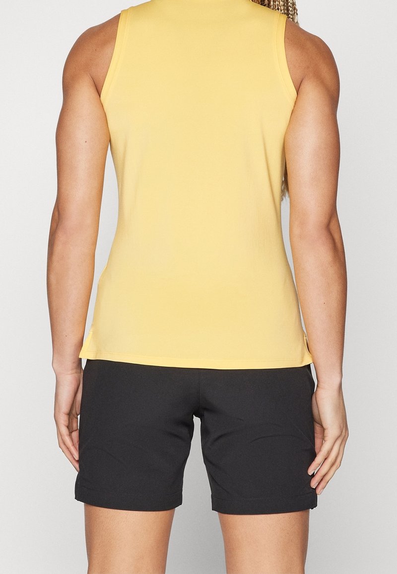 Haut sans manches jaune en tissu léger, associé à un short noir. Le haut présente un col rond et une coupe ajustée.