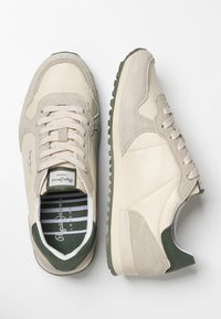 Světlé béžové a zelené semišové tenisky s texturovanými podrážkami, tkaničkami a logem značky na jazyku a vnitřní podrážce, z pohledu shora.