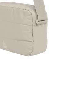 Borsa a tracolla rettangolare beige realizzata in tessuto imbottito, dotata di chiusura con zip e tracolla rimovibile. Logo visibile sul lato.