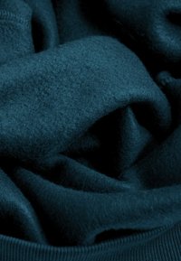 Tijgerkleurige fleece stof gepresenteerd in plooien, die een zachte textuur en een geribbeld rand laat zien. Het materiaal lijkt warm en uitnodigend.