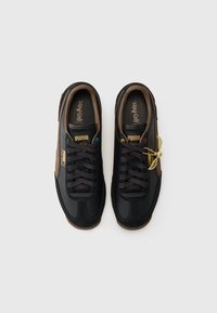 Svart sneakers med brune detaljer, med et gullvingsmerke, mørke snørebånd og flerfargede snøringer på en teksturert såle.
