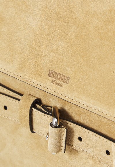 Sārtas zamša rokassoma ar gludu tekstūru, sudraba aparatūru un reljefu "Moschino Milano" logotipu. Iekļauts sprādzes elements ar izšuvuma akcentiem.