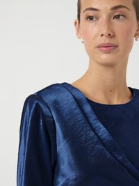 Tengerészkék szatén felső redőzött kialakítással, lekerekített nyakkivágással és strukturált vállakkal. Finoman texturált anyag finom fényű felülettel.