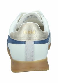 Baskets blanches avec des accents bleu et or, présentant un talon texturé en or, des matériaux contrastants et une semelle en caoutchouc. Logo visible sur le talon.
