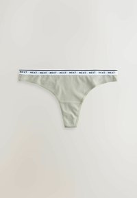 String en coton gris clair avec une ceinture élastique blanche répétant le texte noir "NEXT" sur un fond neutre.