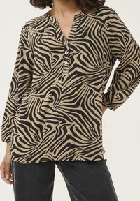 Blouse beige avec imprimé zèbre noir, dotée d'un col en V, d'une patte à quatre boutons et de manches trois-quarts amples. Texture de tissu douce.