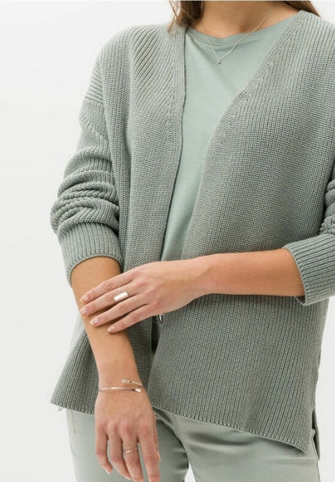 Person som bär en ljusgrön stickad cardigan, matchande topp och byxor, med silverringar, armband och ett fint halsband.