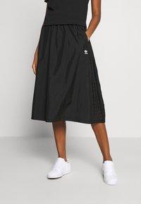 Svart midikjol med elastisk midjeband, med sidopaneler med ett strukturerat mönster och en liten vit logotyp. Matchad med vita sneakers.