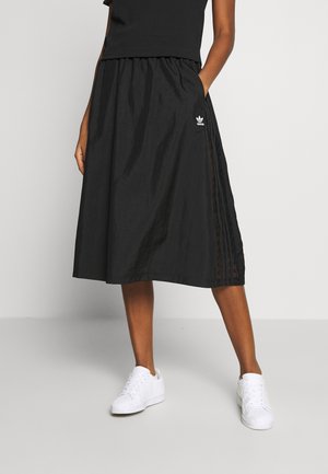 Svart midikjol med elastisk midjeband, med sidopaneler med ett strukturerat mönster och en liten vit logotyp. Matchad med vita sneakers.