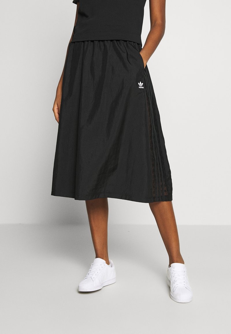 Svart midikjol med elastisk midjeband, med sidopaneler med ett strukturerat mönster och en liten vit logotyp. Matchad med vita sneakers.