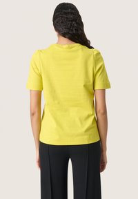 Yellow short-sleeve t-shirt with a crew neck, fitted silhouette, and soft cotton fabric, paired with black wide-leg trousers.