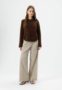 Brauner Strickpullover mit rundem Ausschnitt und langen Ärmeln, kombiniert mit hellbeigen, weit geschnittenen Hosen und schwarzen Sandalen mit Absatz.