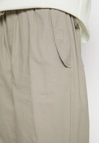 Pantaloni cargo beige chiaro con tasca a soffietto sul lato, indossati con una camicia bianca leggermente infilata nella vita.