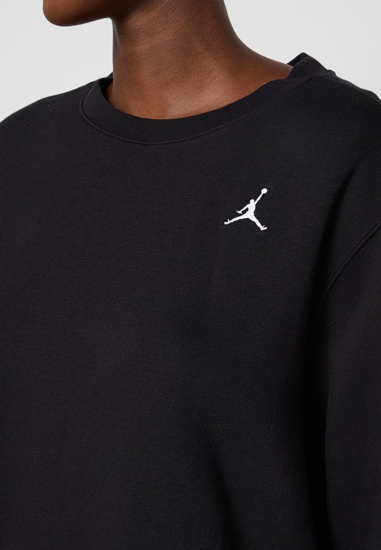 Sudadera negra de algodón, con cuello redondo ribeteado y un logo Jumpman blanco en el lado izquierdo del pecho. Textura suave, diseño minimalista.