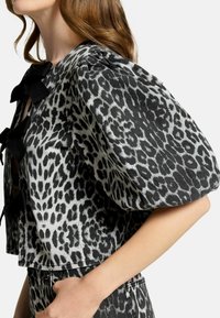Giacca cropped in stampa leopardo bianca e nera, con maniche a sbuffo e dettaglio a fiocco legato al collo. Tessuto texturizzato.