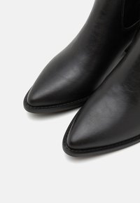 Bottines noires à bout pointu, fabriquées en matériau synthétique lisse. Présentent des coutures le long des bords et une semelle basse et plate.