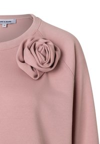 Sweatshirt rose à motif avec un fond rose clair, doté d'un col rond et d'un accent floral texturé sur le côté gauche. Tissu doux avec une coupe décontractée.
