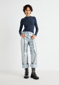 Top lung cu maneci lungi navy cu textura, blugi metalici argintii cu picioare largi și margini rulabile, și cizme negre de tip combat cu multiple catarame.