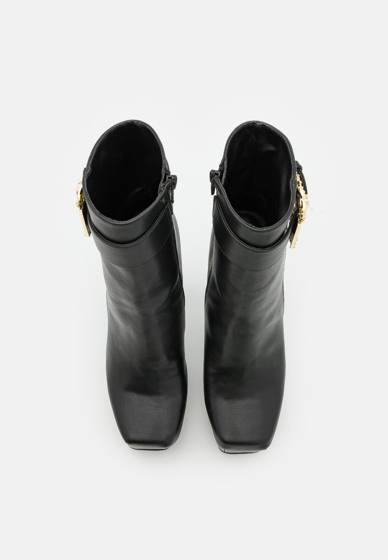Stivali neri in pelle fino alla caviglia con punta affusolata, texture liscia e dettagli in metallo dorato sul lato. Tacco quadrato a blocco.
