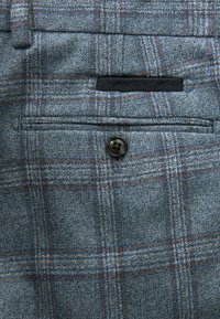 Blaues Karostoffmuster mit orangefarbenen Akzenten, ausgestattet mit einer Vordertasche mit einem schwarzen Knopf und einer glatten Textur für ein strukturiertes Design.