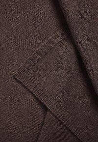Écharpe en tricot marron avec une texture douce ; elle présente un bord côtelé et un motif de tissage lâche. Le tissu semble chaud et confortable.