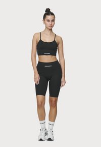 Top corto deportivo negro y pantalones cortos ajustados a juego con marca blanca. Tela suave y elástica, diseño minimalista. Calcetines y zapatos deportivos blancos.