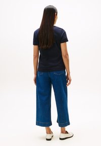 Granatowy t-shirt z krótkim rękawem w połączeniu z szerokimi, wysokim stanem niebieskimi dżinsami z surowym obszyciem i jasnym wypraniem. Widać casualowe obuwie.