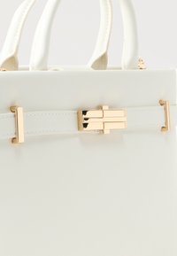 Λευκή δερμάτινη τσάντα χειρός με διπλές λαβές και χρυσή ορθογώνια αγκράφα στη μπροστινή λουρίδα.