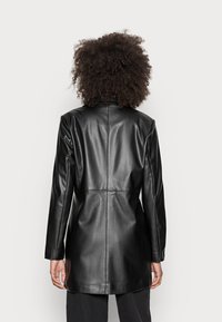 Blazer in pelle nera con maniche lunghe e vestibilità strutturata. Texture liscia, design elegante e dettaglio con cucitura posteriore.