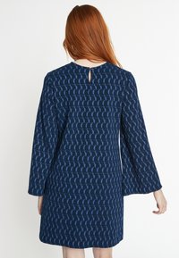 Marineblaues Kleid mit strukturiertem Muster und blauen Akzenten, Dreiviertelärmel und einer Schlüsselrinne am Rücken.