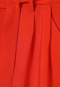 Rode stof met een gladde textuur, voorzien van plooien en een gestrikt ceintuur in de taille. De kleur is levendig en gelijkmatig verzadigd.