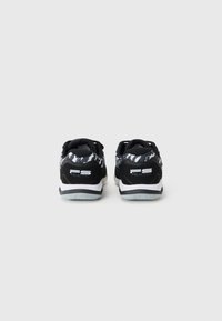 Black and white athletic shoes featuring a textured upper, padded collar, and rubber outsole with a prominent logo on the heel.