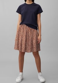 T-shirt navy a maniche corte abbinato a una gonna color ruggine con un motivo a pois bianchi. Modella che indossa sneakers bianche.