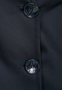 Twee glanzende zwarte knopen met vier gaten genaaid op donkere stof, met tekst gegraveerd rondom de randen van de knopen.