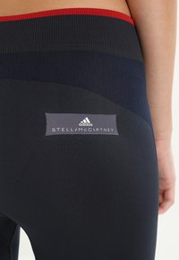 Marina stretchleggings med en kontrasterande röd midja, med en logotyp patch i grått med "STELLA McCARTNEY" och "adidas" branding.