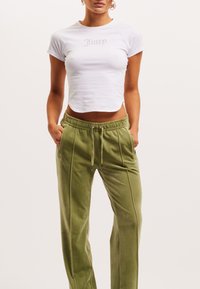 Valge lühike T-särk, millel on halli värvi "Juicy" tikand, koos oliivroheliste, pehmete, laia säärega joggeritega, millel on elastne vöökoht ja taskud.